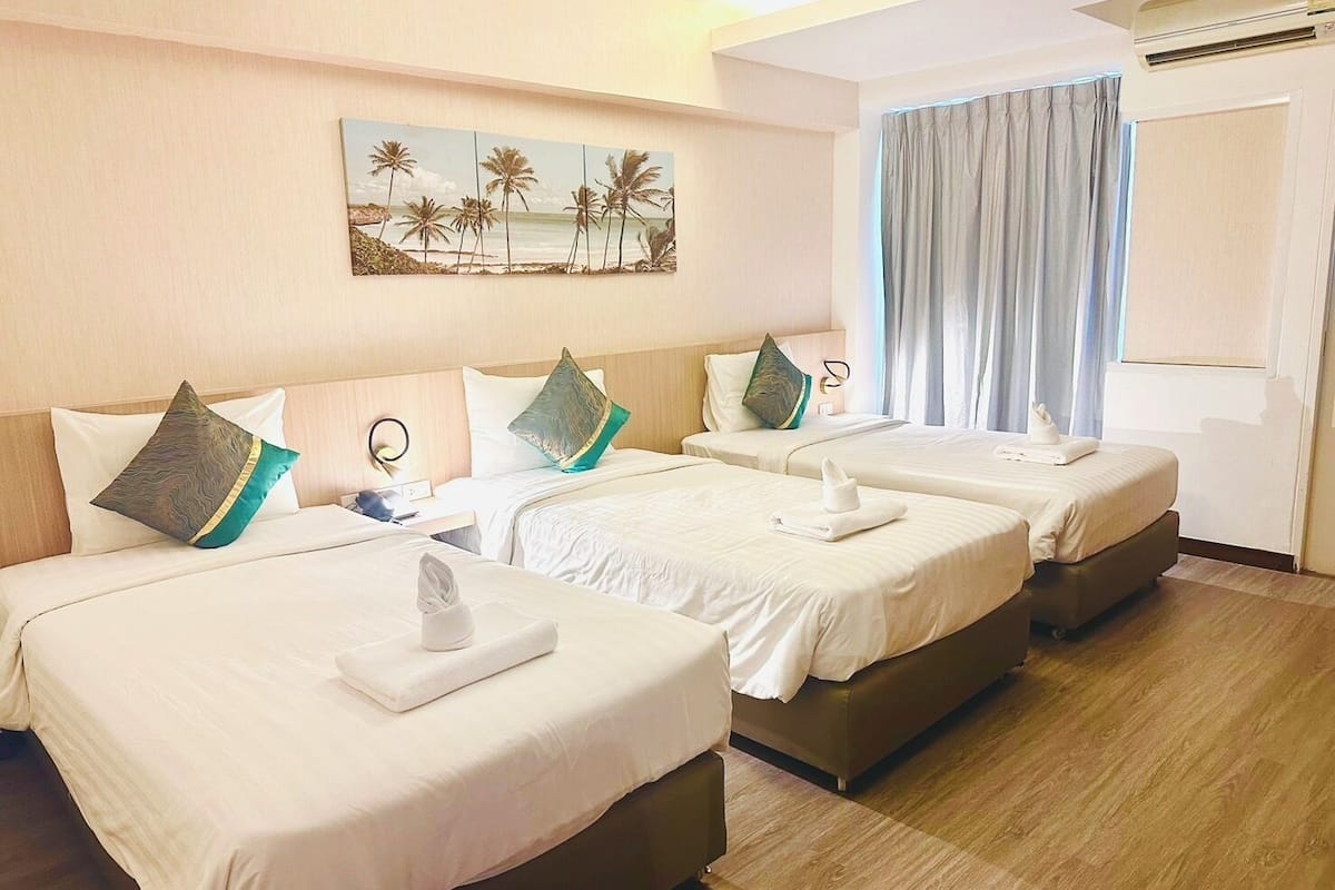 A hotel room with three beds, a painting of palm trees, an air conditioning unit, and a window with curtains.