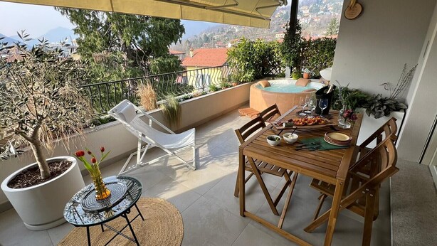 Een balkon met een eettafel, stoelen, een klein rond tafeltje met een vaas en een bloempot.