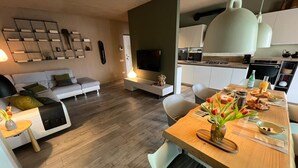 Een moderne woonkamer met een bank, televisie en een eethoek met een houten tafel gedekt voor het ontbijt.
