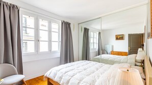 A bedroom with a bed, a chair, a mirror, and a window with curtains.