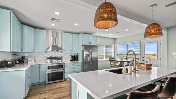 A modern kitchen with light blue cabinets, stainless steel appliances, a large island, and wicker pendant lights.