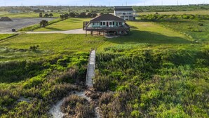 A large house with a porch and a covered patio area, surrounded by a grassy field and a dirt path leading to the house.