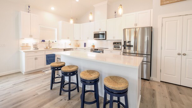 A modern kitchen with white cabinets, stainless steel appliances, and a central island with bar stools. - Get ready to soak up the sun at Villa Caman! (Galveston)