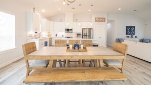 A modern kitchen with white cabinets, a central island, and a dining area with a wooden table and chairs. - Get ready to soak up the sun at Villa Caman! (Galveston)