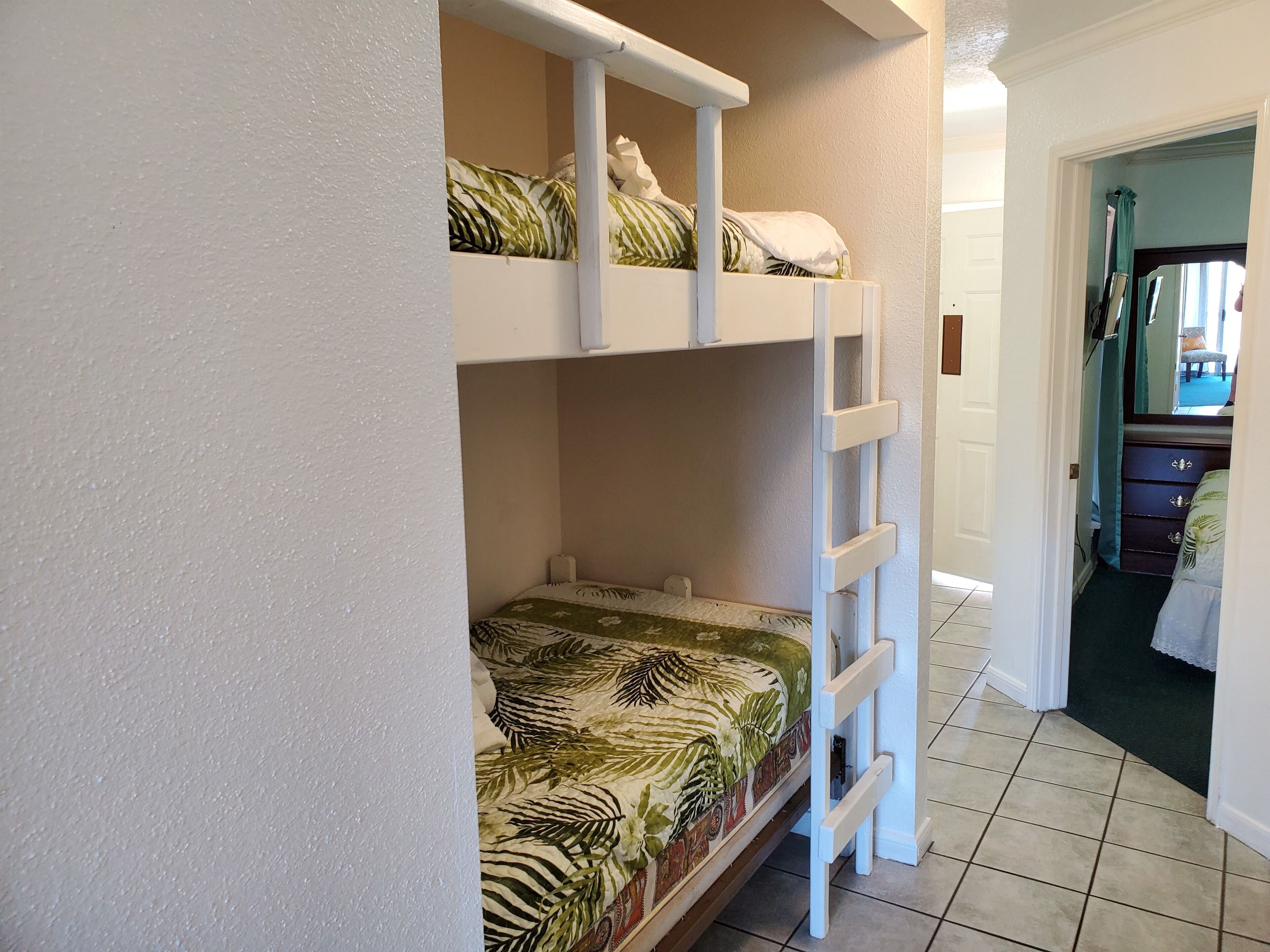 A bunk bed with a tropical leaf-patterned bedspread, white headboard, and a white ladder.