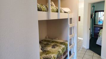 A bunk bed with a tropical leaf-patterned bedspread, white headboard, and a white ladder.