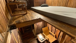 Una habitación pequeña de madera con una cama, una mesita con lámpara y una silla.