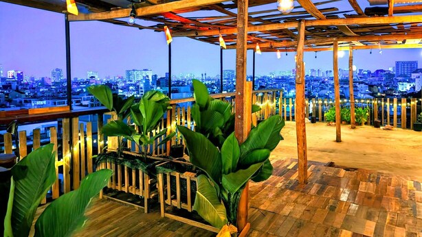 Una terraza en la azotea con suelo de madera, plantas en macetas y vistas a la ciudad al anochecer.