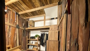 Una habitación rústica con paredes y suelos de madera, un banco de madera, una mesita con un objeto verde y una estantería con diversos objetos.