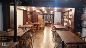 Un restaurante acogedor con mesas y sillas de madera, una barra alargada y estanterías con juegos de mesa.