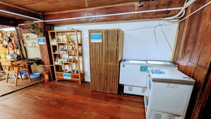 Una habitación con suelo de madera, un estante de madera con varios objetos, un refrigerador blanco y un separador de madera.