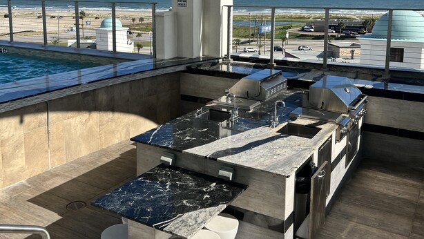A rooftop bar with a pool view, bar counter, and white stools. - Good Day Sunshine - Emerald 712 (Galveston)