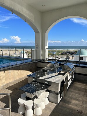 A rooftop bar with a pool view, bar counter, and white stools. - Good Day Sunshine - Emerald 712 (Galveston)