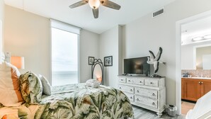 A bedroom with a large bed, a dresser, a television, and a view of the ocean. - Good Day Sunshine - Emerald 712 (Galveston)