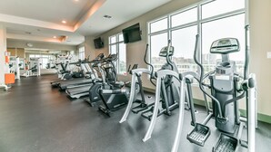 A gym with various cardio machines, a television, and large windows offering a city view. - Good Day Sunshine - Emerald 712 (Galveston)