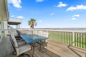 A wooden deck with a glass table and chairs, a white railing, and a view of the ocean. - Original Margaritaville Beachfront Paradise Found. (Galveston)