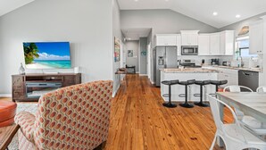 Una cocina moderna con armarios blancos, una isla central con taburetes y una zona de comedor con una mesa y sillas blancas.