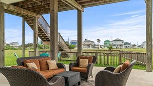 Un patio exterior con mobiliario de mimbre, una escalera de madera y vistas a casas al fondo.