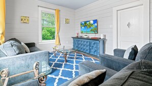 Een woonkamer met een blauw-wit gestreept tapijt, een blauwe mediameubel en een televisie die aan de muur is bevestigd.