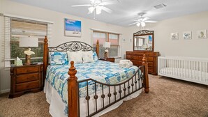 Une chambre à coucher comprenant un lit, des tables de chevet, une commode, un berceau et des ventilateurs de plafond.