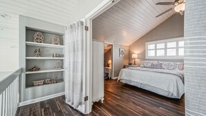 Et soveværelse med skråvæg, seng, natbord, lampe og en reol med pynteting.