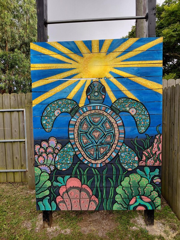 A wooden fence with a painted mural of a turtle and sun. - Sandy Turtle-Gone to the Beach, Be Back Never! (Galveston)