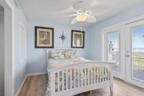 Ein Schlafzimmer mit einem weißen Bett, einem Deckenventilator und einer Tür, die auf einen Balkon führt.
