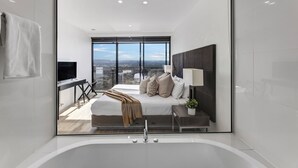 A modern bedroom with a large bed, a bedside table with a lamp, and a view of the city through large windows. - Circle on Cavill River View (Surfers Paradise)