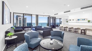 A modern lounge area with seating and a bar, large windows with a view of the sea and buildings, and a clean, contemporary design. - Circle on Cavill River View (Surfers Paradise)