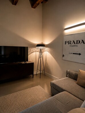 A living room with a television, a lamp, a sofa, and a wall sign.