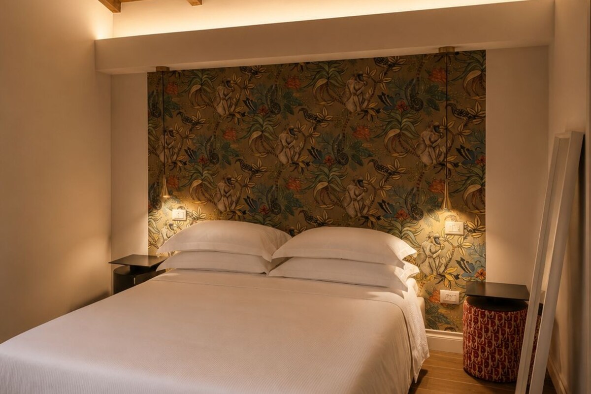 Une chambre avec un plafond en bois, un lit avec une literie blanche, une table de chevet, une lampe et un papier peint à motifs.
