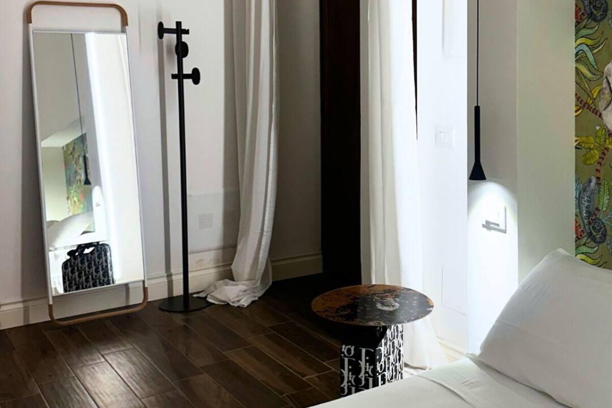 Ein modernes Schlafzimmer mit einem Bett, einem Spiegel, einer Stehlampe und einem kleinen runden Tisch.