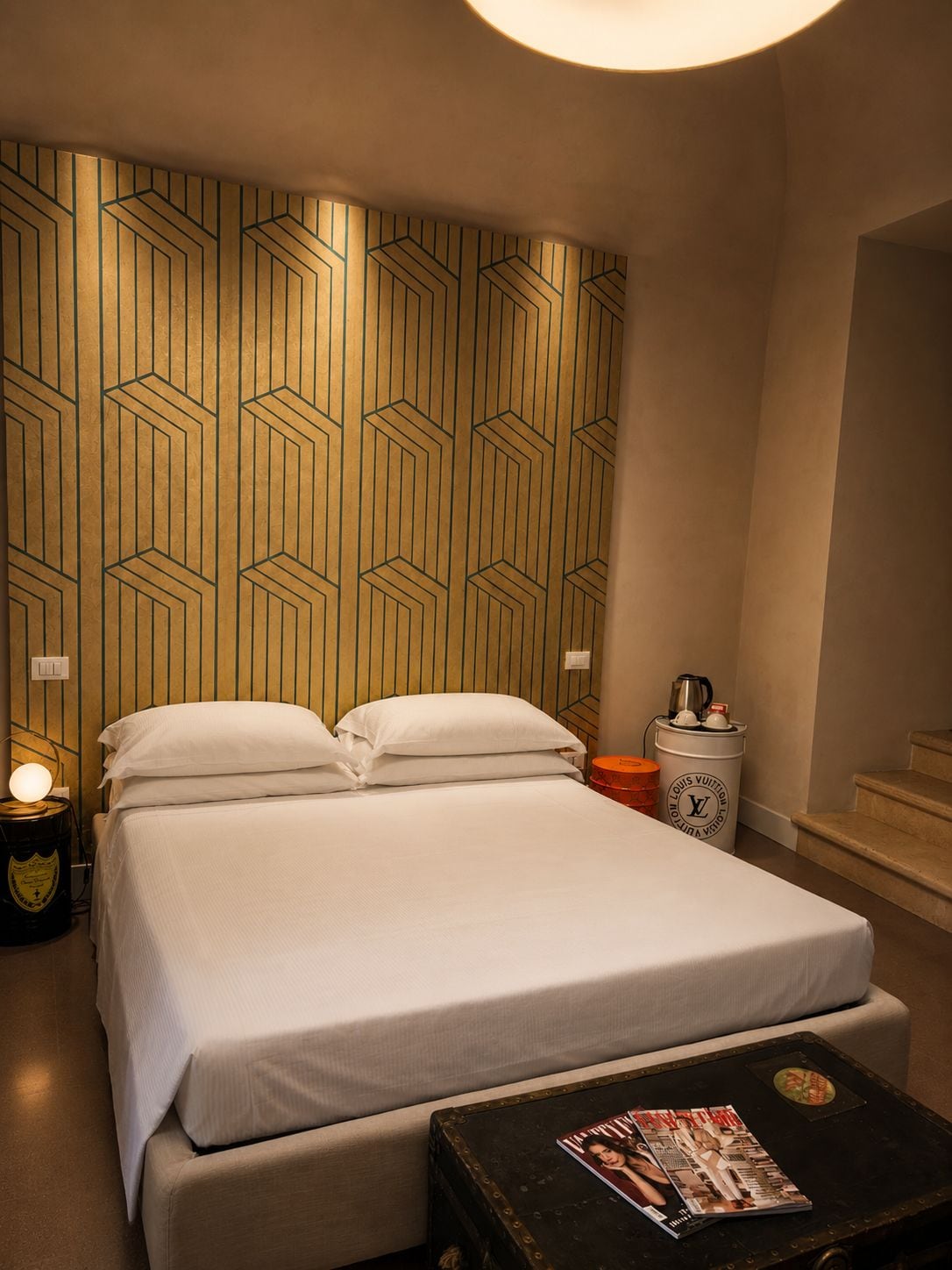 A hotel room with a bed, bedside table, lamp, and a magazine on a small table.