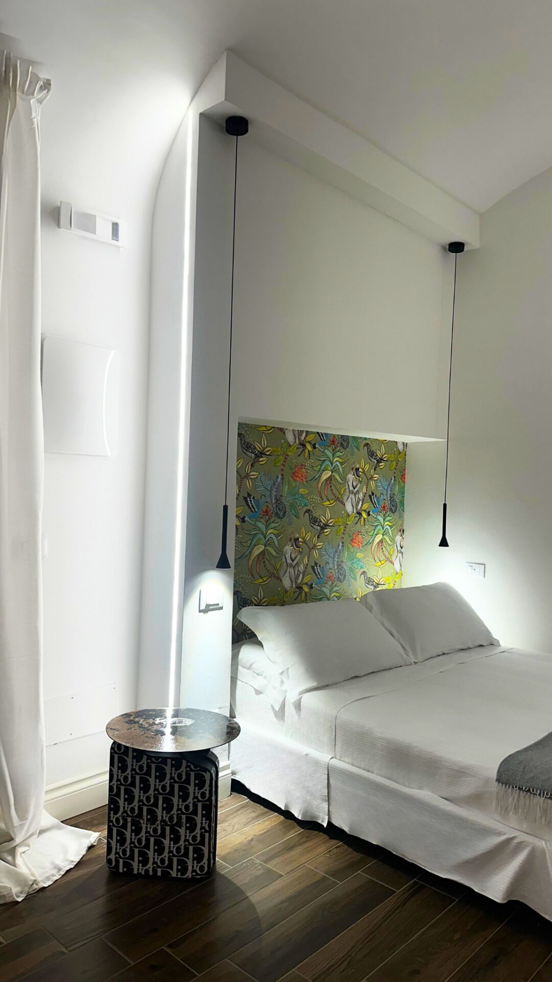 Un dormitorio moderno con una cama, una mesita auxiliar redonda, un cabecero colorido y lámparas colgantes.