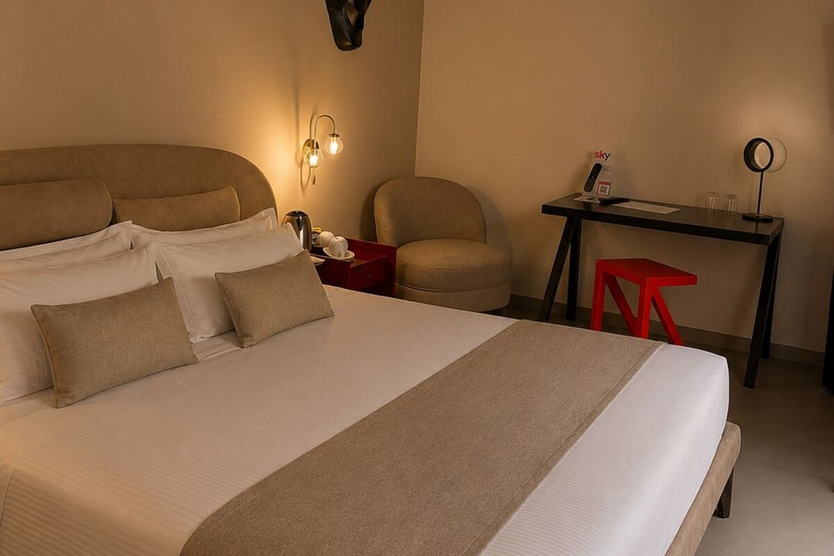 Une chambre d’hôtel avec un grand lit, un bureau, une chaise et un luminaire fixé au mur.