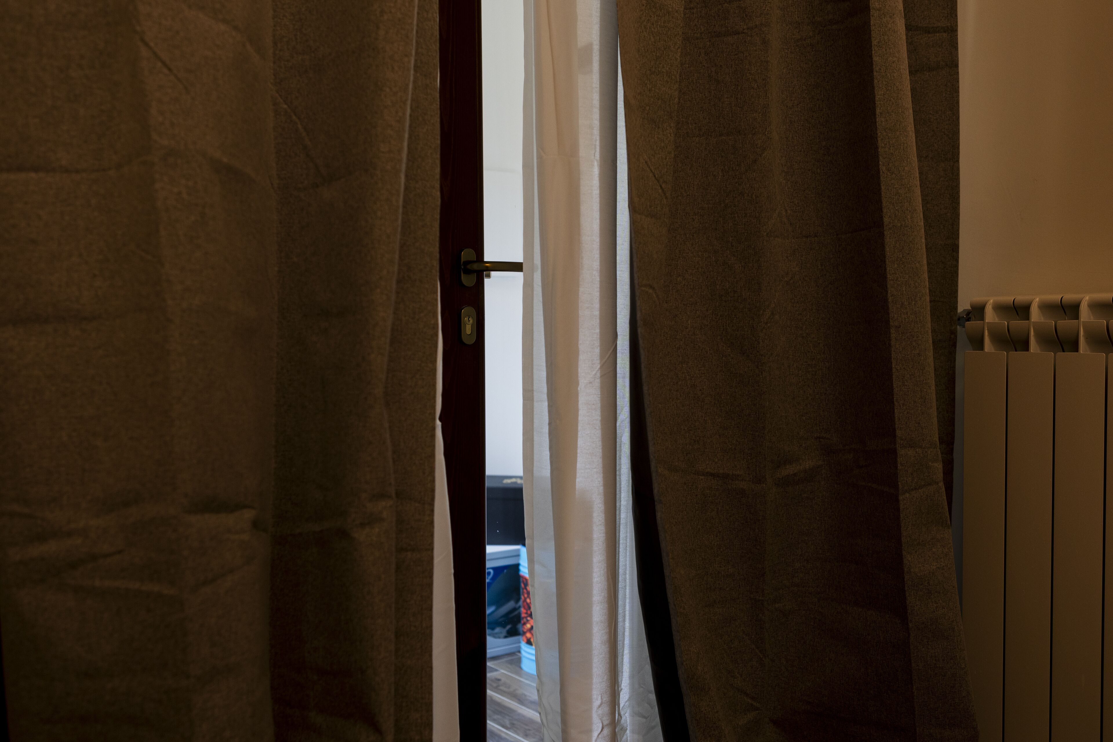 Ein Durchgang mit Vorhängen, einem Heizkörper und einem Blick in einen Raum mit Bett und Koffer.