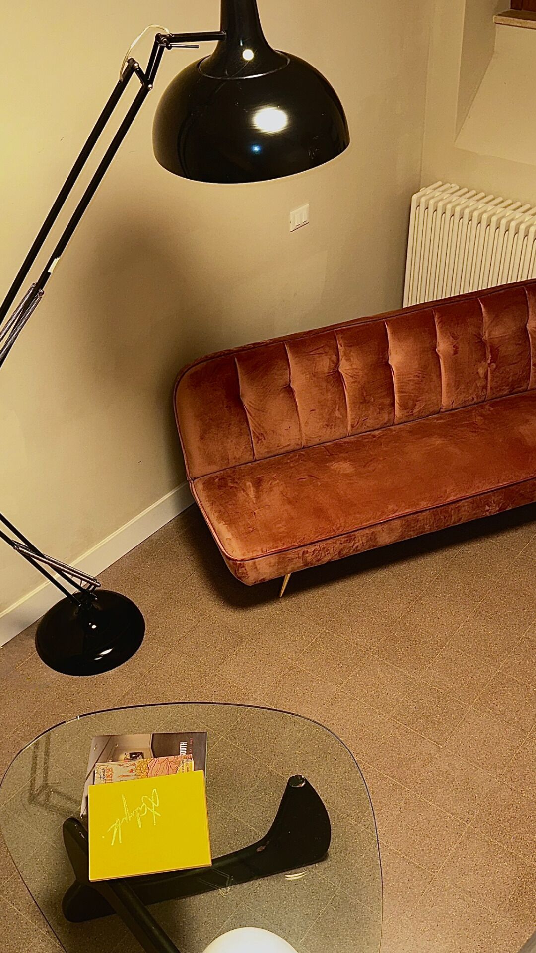 Ein Wohnzimmer mit einem braunen Sofa, einer schwarzen Stehlampe und einem Glastisch mit einer gelben Karte.