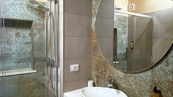 A modern bathroom with a glass shower enclosure, a white sink with a marble backsplash, and a large round mirror.
