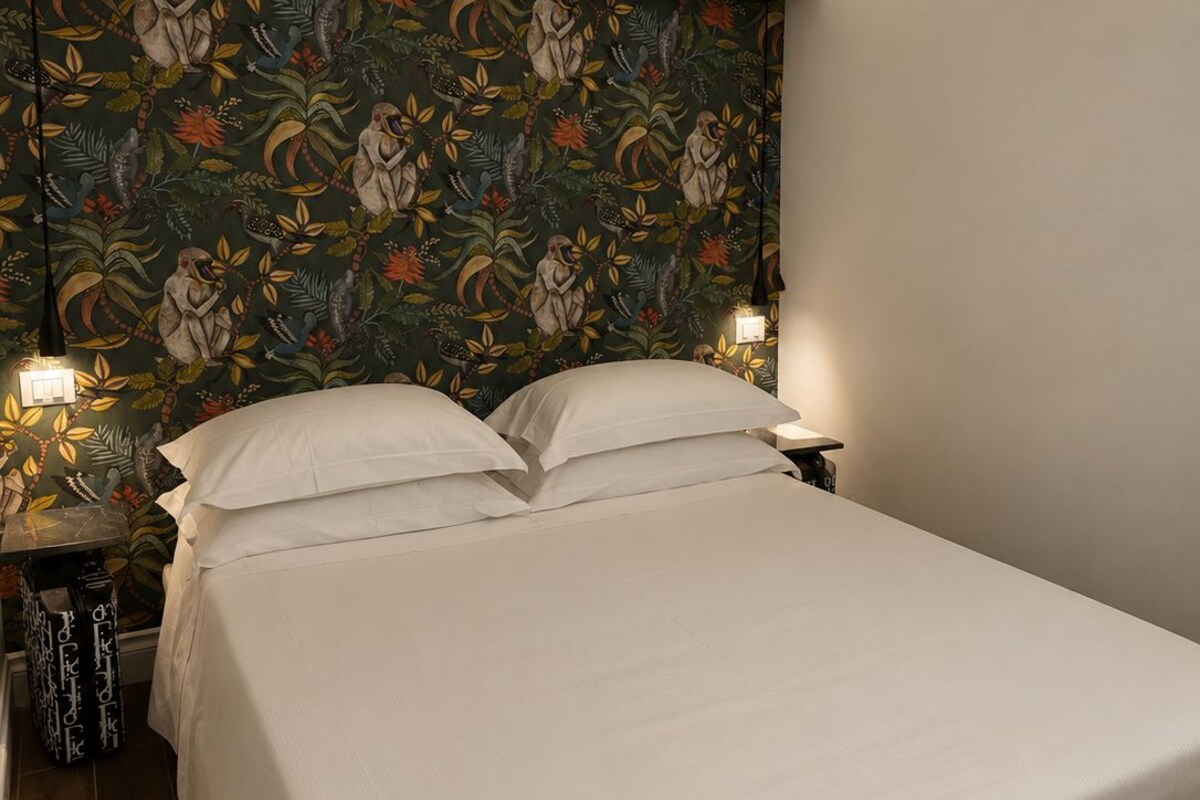 Une chambre à coucher avec un lit, deux tables de chevet et un mur orné d’un motif floral.