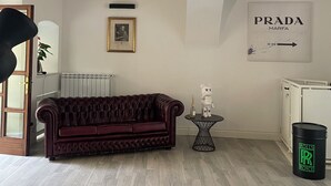 Een kamer met een donkerrode bank, een klein rond tafeltje met een kaars en decoratie, een radiator, en een bordje met Prada Marfa.