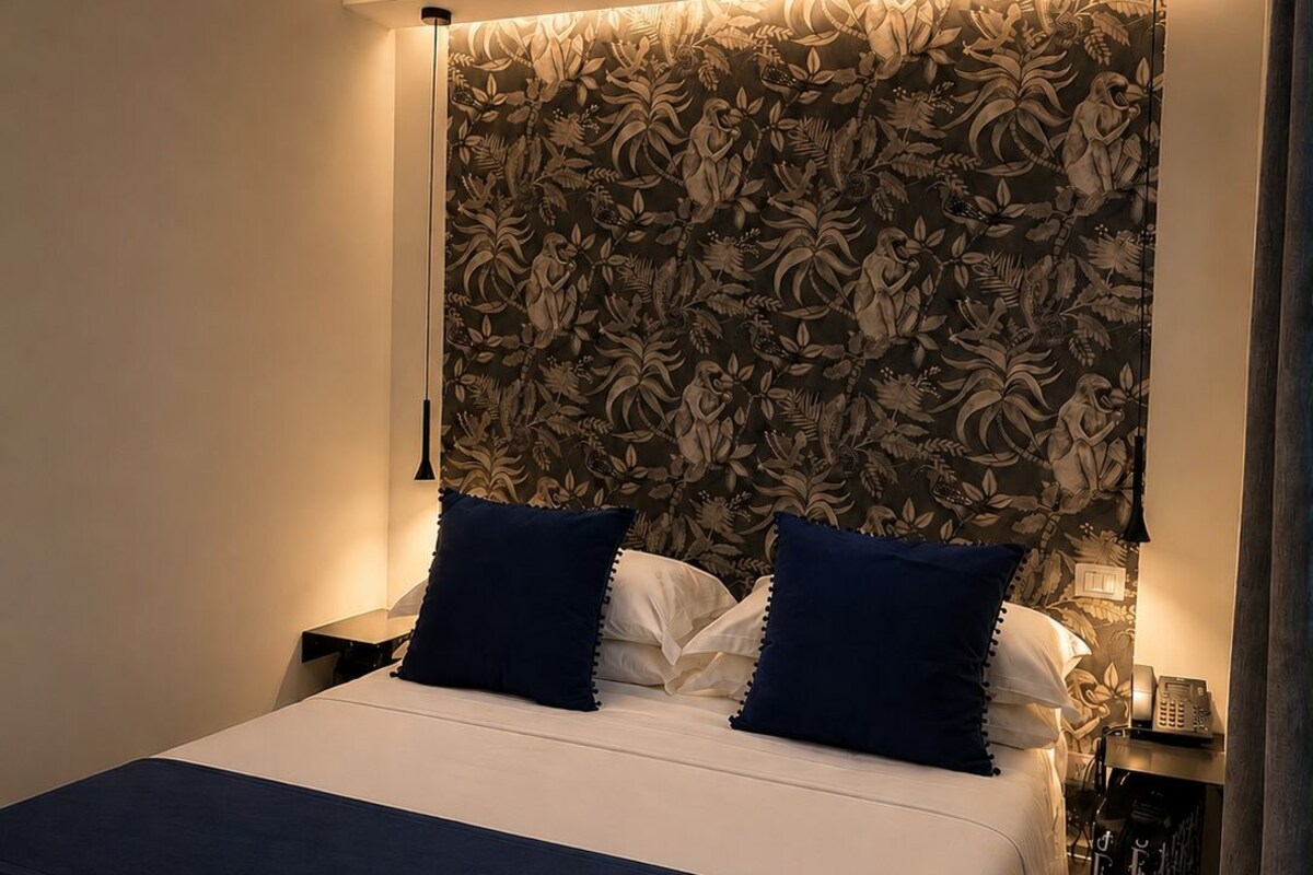 Une chambre d’hôtel avec un grand lit, une tête de lit à motifs floraux, des lampes de chevet et un téléphone sur une table de chevet.