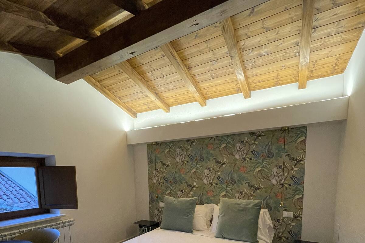 Ein Schlafzimmer mit einem großen Bett, einem Fernseher auf einem Schrank, einem kleinen Tisch und einem Wandpapier mit Muster.