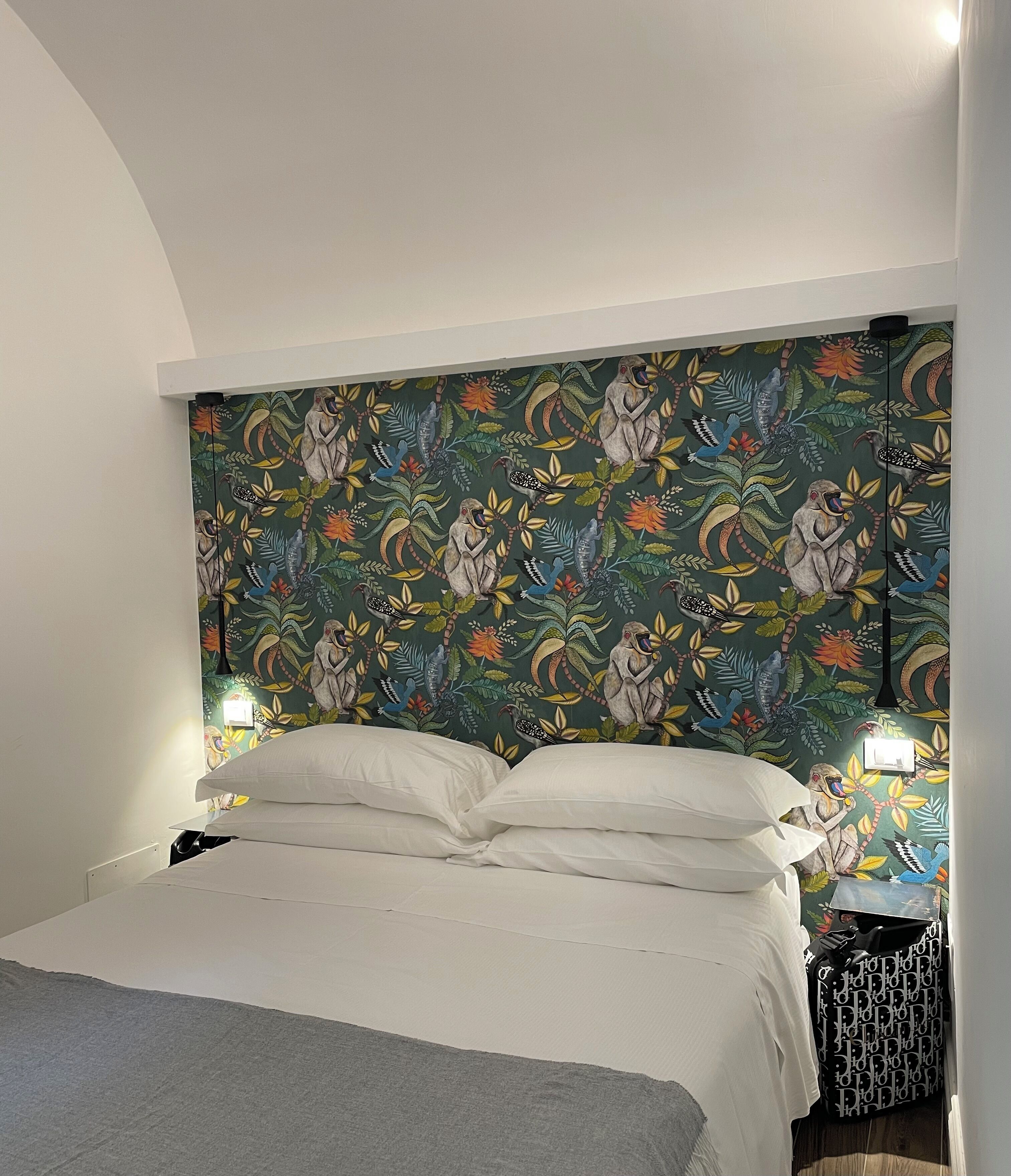Una cama bien hecha con ropa blanca, un cabecero estampado en verde y dos lámparas de noche.
