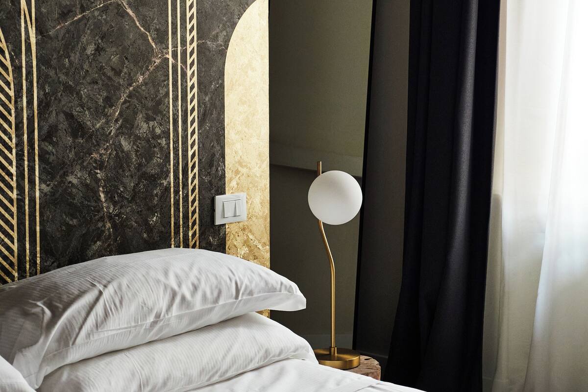 Ein Schlafzimmer mit einem Bett, Kissen, einem Nachttisch, einer Lampe, einem Spiegel und einer Wand mit Marmoroptik.