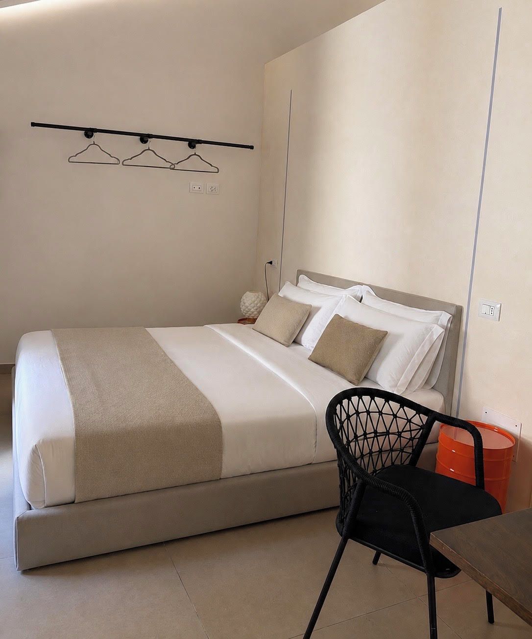 A bedroom with a bed, a chair, a table, and a wall-mounted hanger rack.