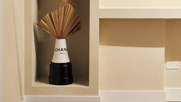 Un vase blanc avec une base noire portant l’inscription « CHANEL PARIS », le tout placé sur un mur de couleur beige.