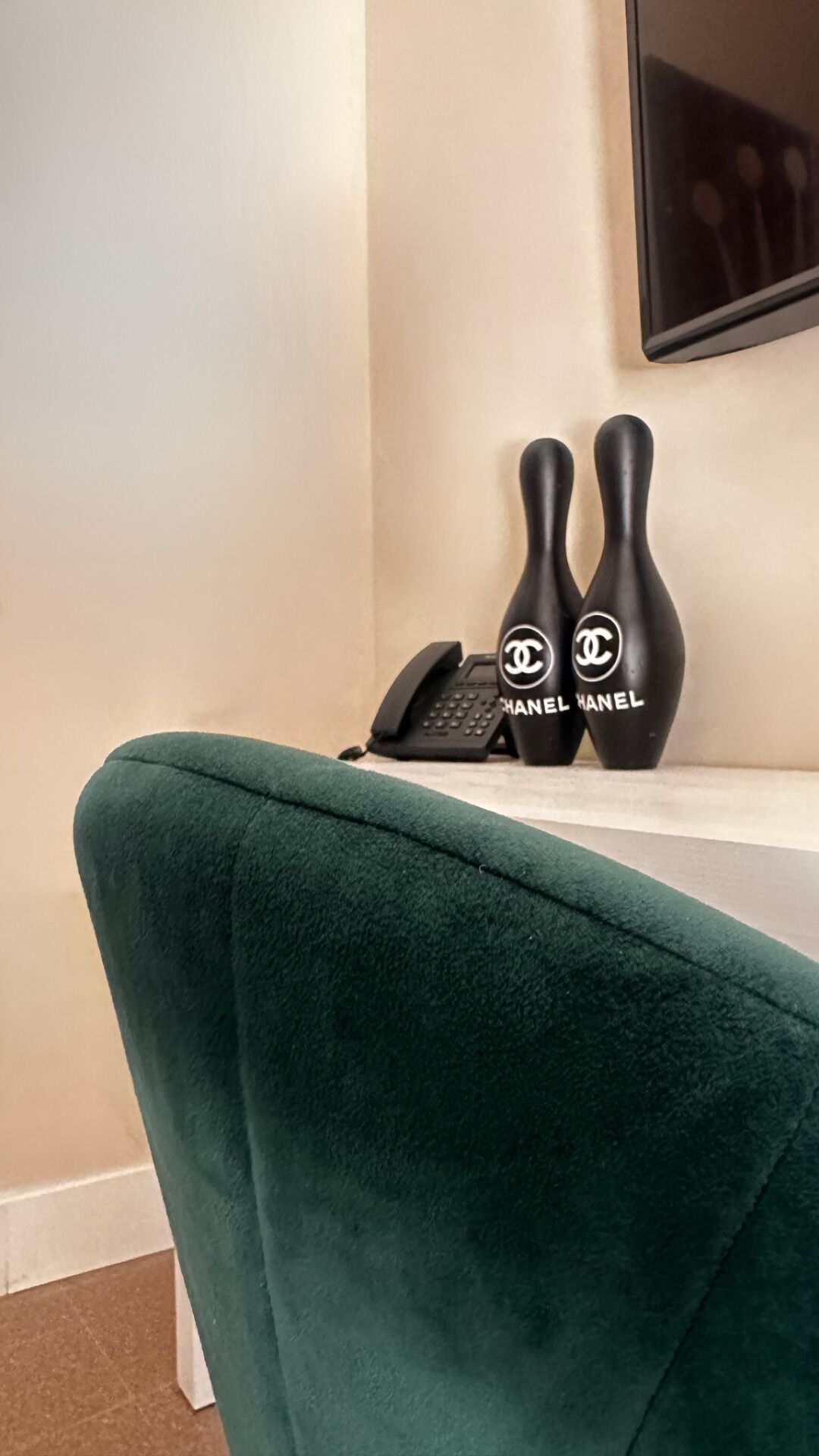 A green chair with a telephone and two black vases with the Chanel logo on a white surface.