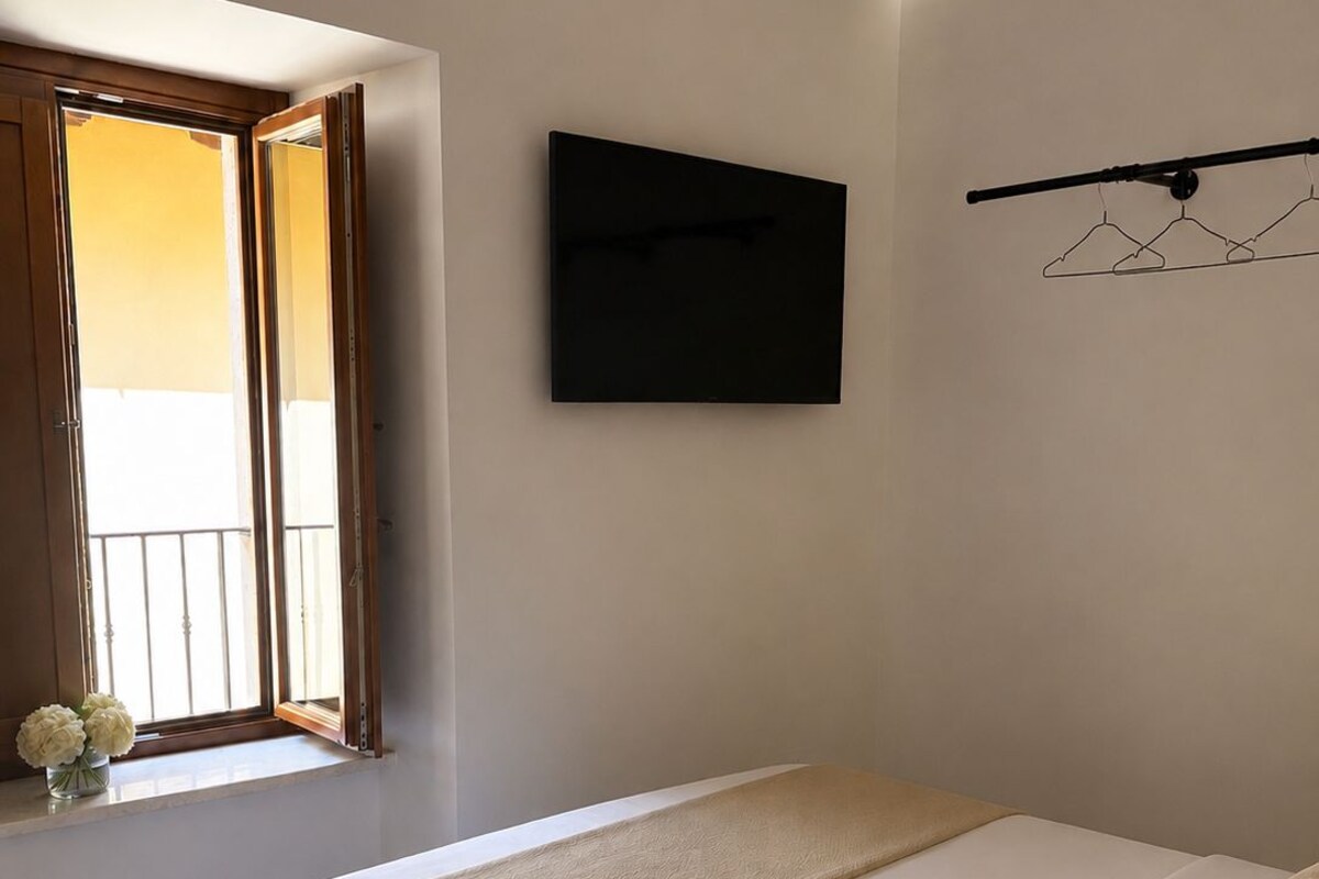 Une chambre à coucher avec un lit, une fenêtre avec des rideaux, un téléviseur fixé au mur et un luminaire au plafond.