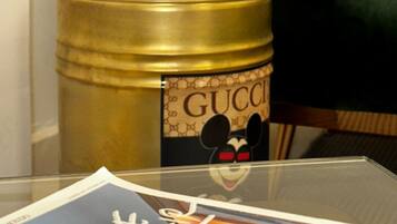 A glass table with a magazine, a gold-colored container with a Gucci label, and a dark green chair.