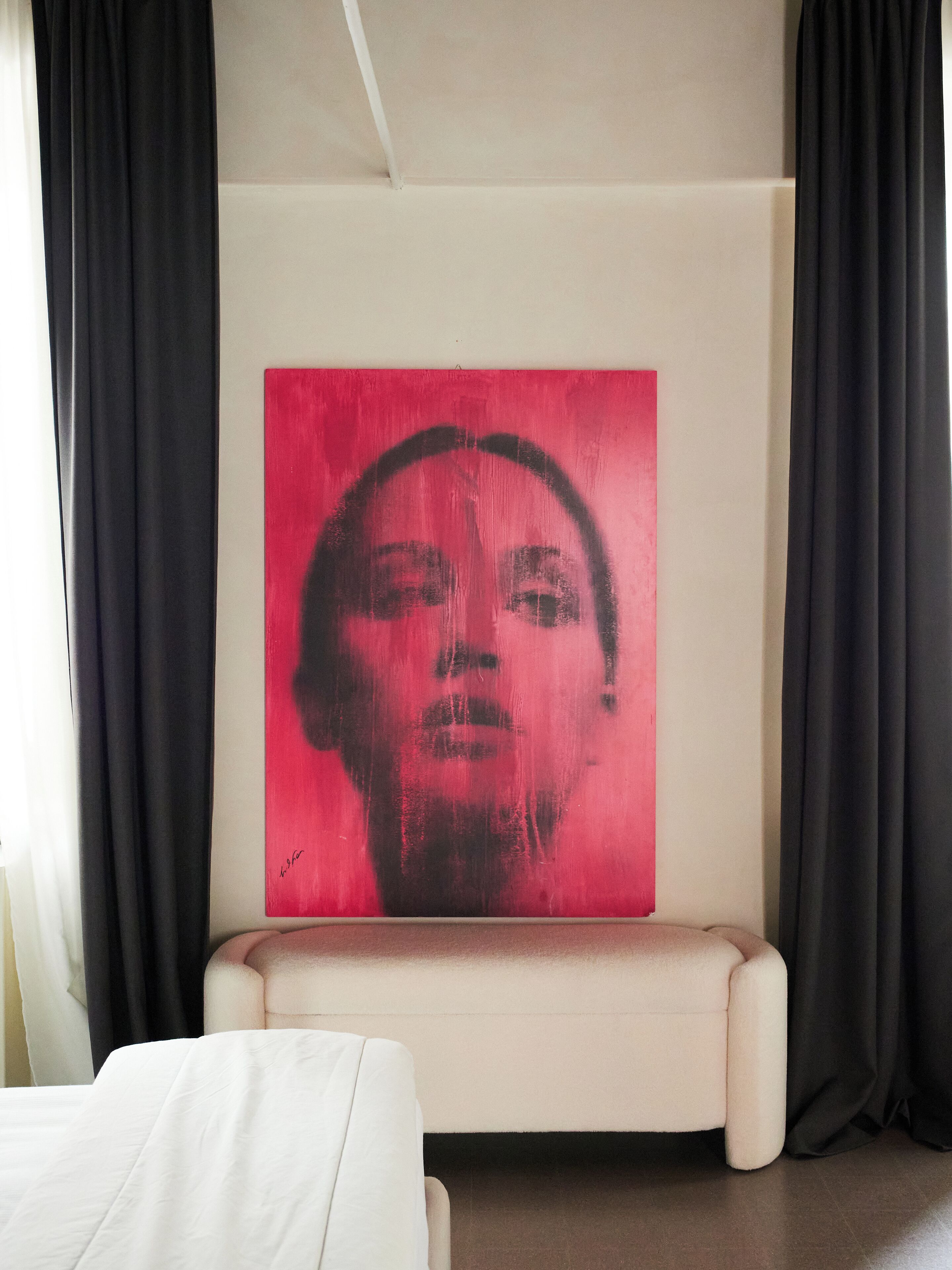 A room with a large red artwork on the wall, a white sofa, and black curtains.